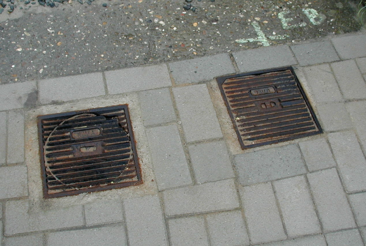 Twee rioleringsputjes naast elkaar op een voetpad.